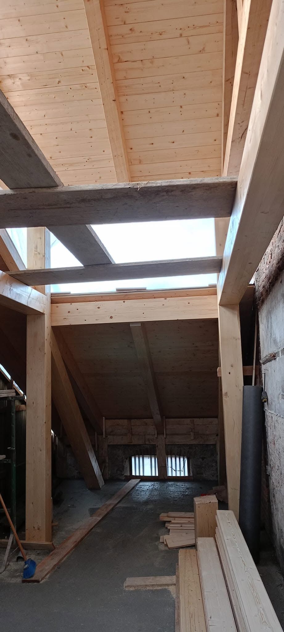 Interno di un cantiere edile con travi di legno inclinate e un lungo e stretto corridoio che si apre verso la luce.