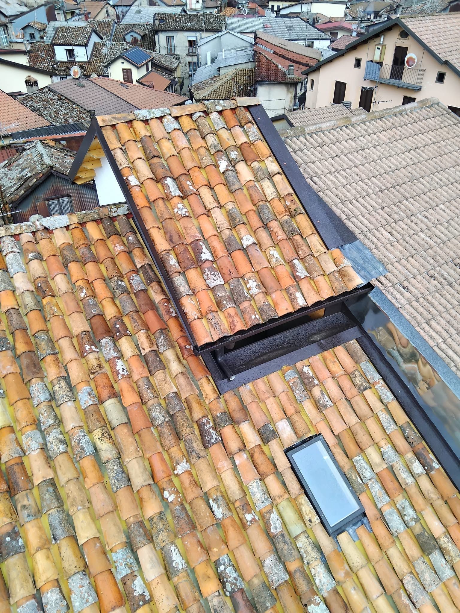 Tetti di tegole rosse in un denso borgo collinare, con lucernari e comignoli visibili.