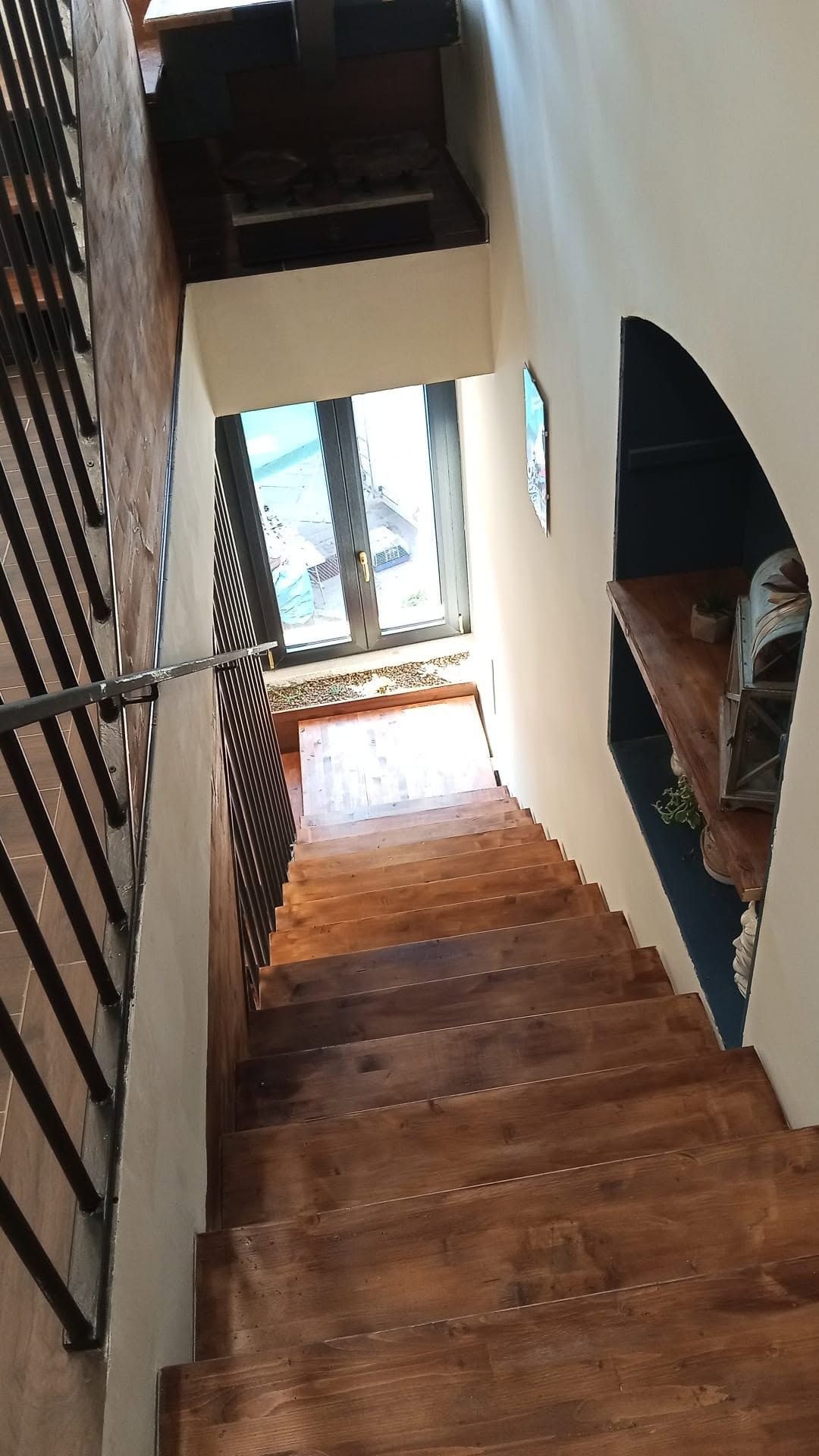 Scala interna con gradini in legno e pareti bianche che conduce a un ingresso luminoso.