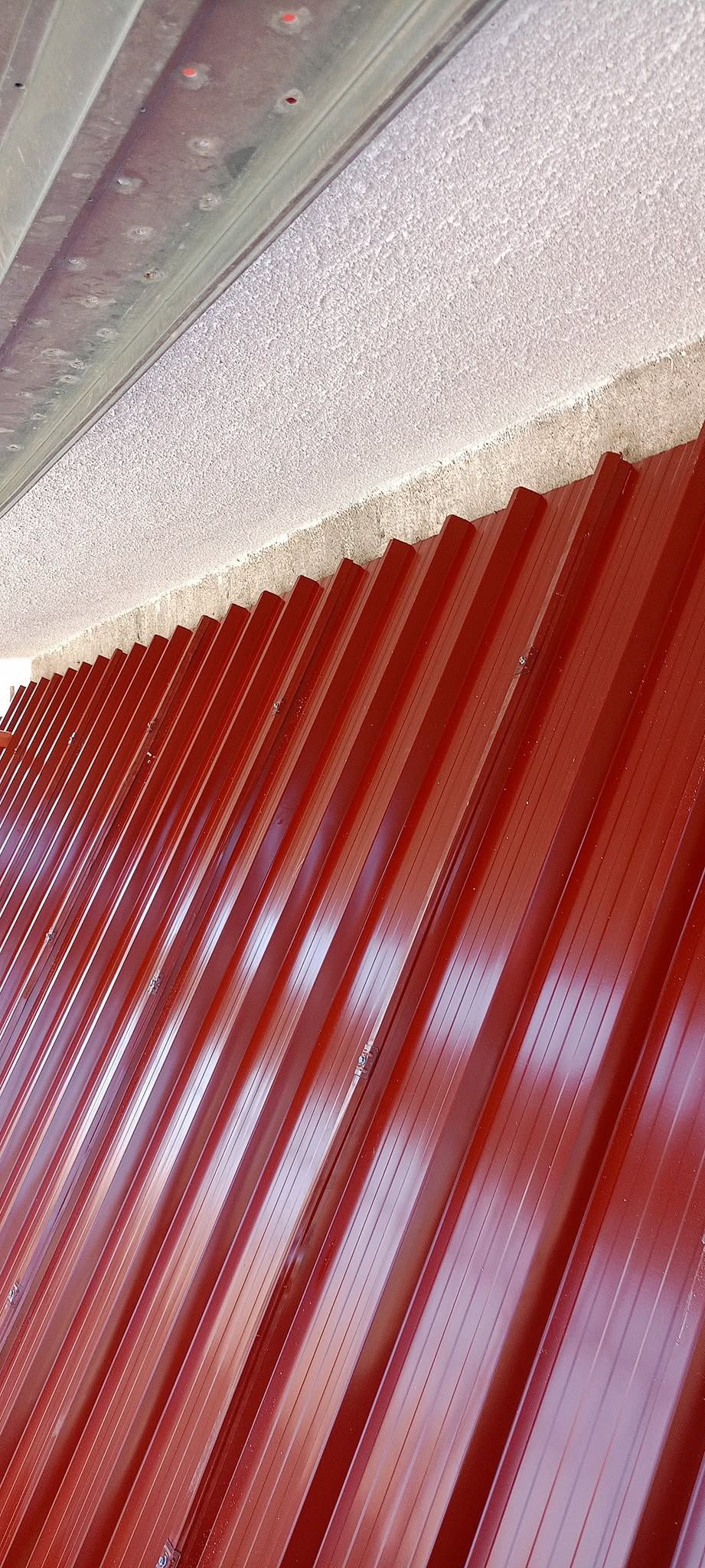 Primo piano di un tetto in lamiera ondulata rossa sotto un soffitto bianco con trama.