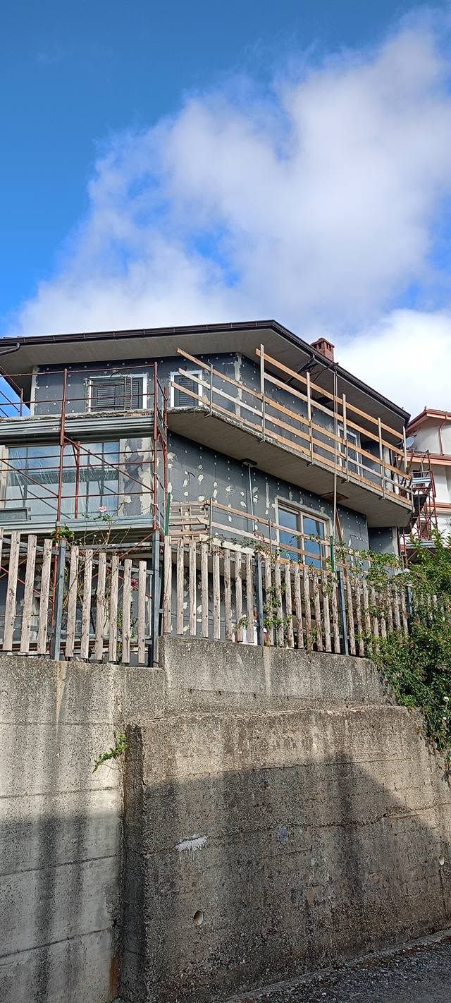 Casa consumata dal tempo con rivestimento blu su un muro di cemento sotto un cielo azzurro brillante.