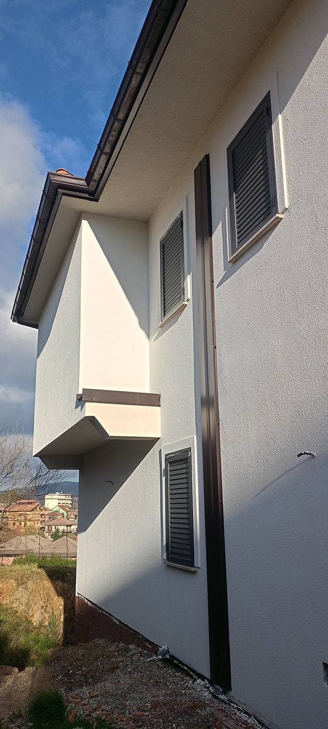Esterno di una casa bianca con un piccolo balcone, finestre e tetto spiovente sotto un cielo azzurro.