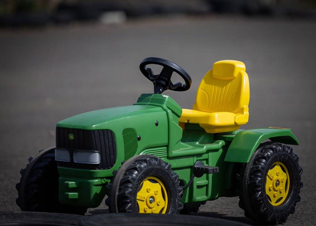 A green and yellow toy tractor is sitting on the ground.