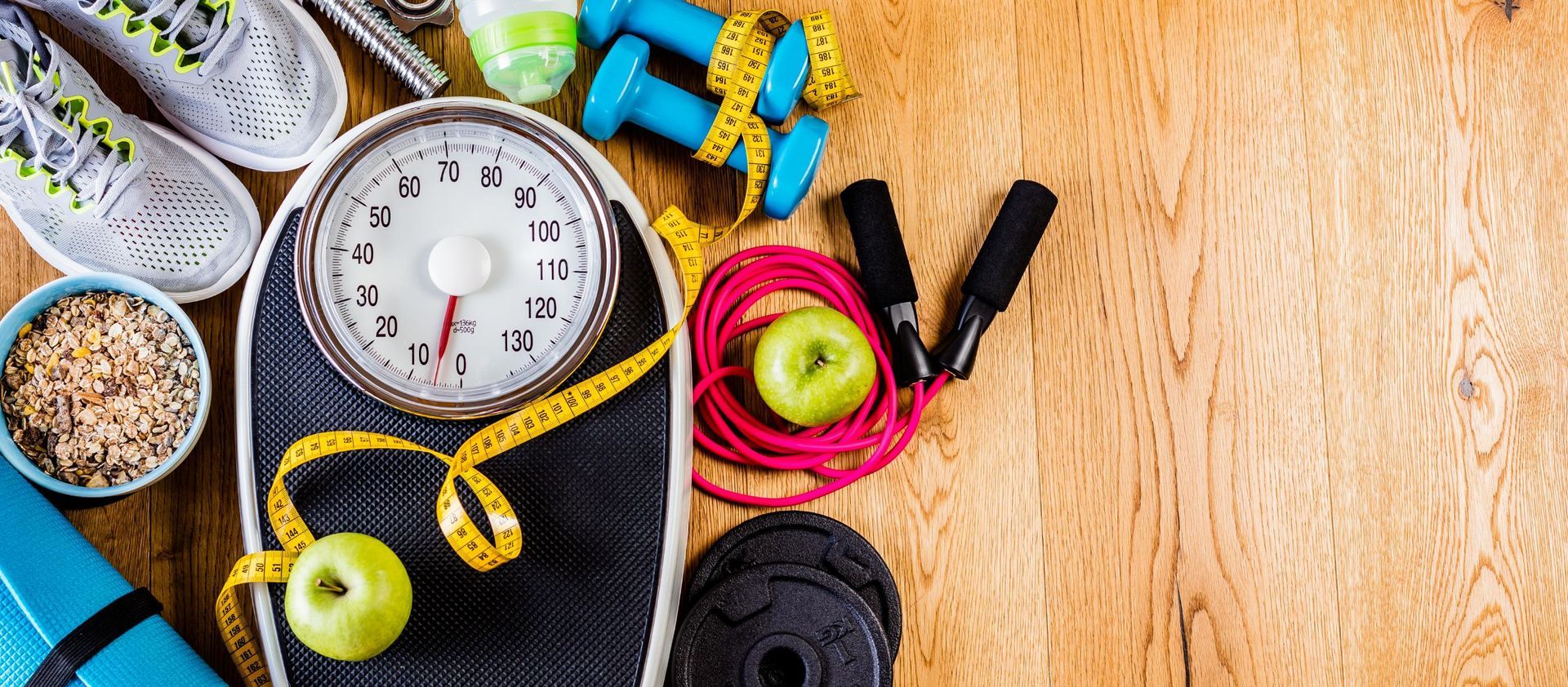 Fitness equipment and healthy food on a wooden surface. Includes a scale, weights, shoes, and apples.