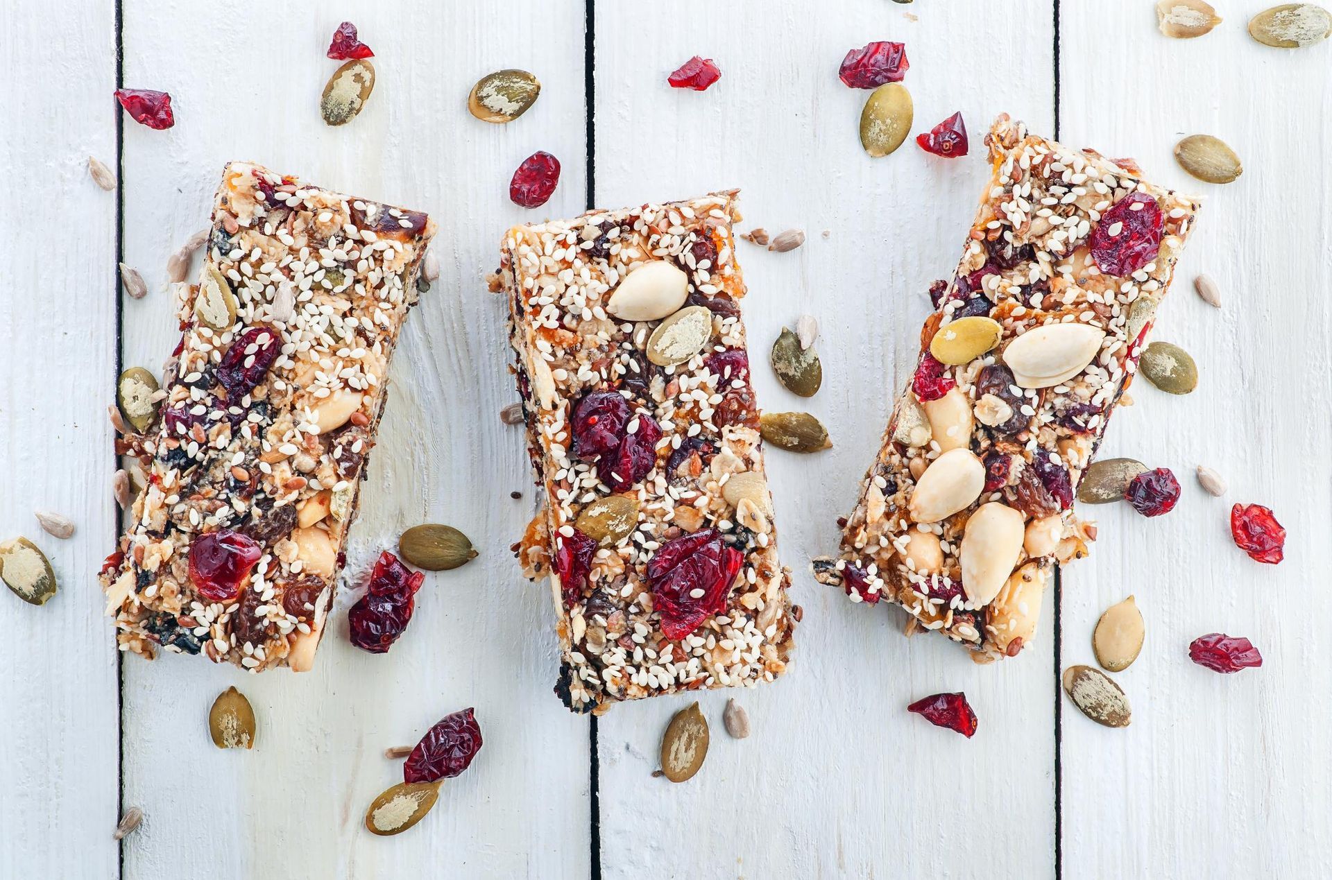 Three granola bars with nuts and dried fruit on a white wooden surface.