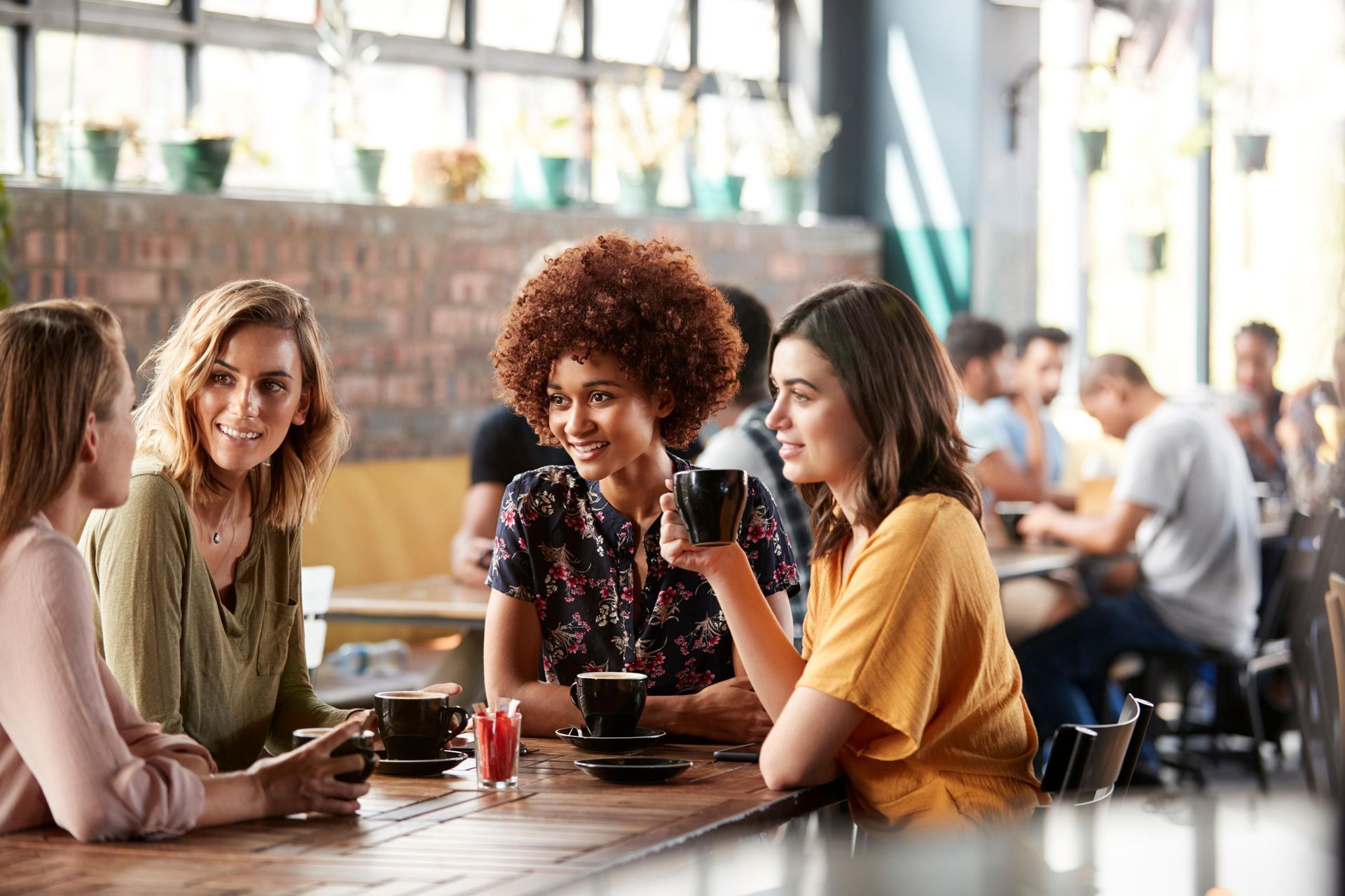 Four people seated at a table in a cafe, talking and holding coffee cups.
