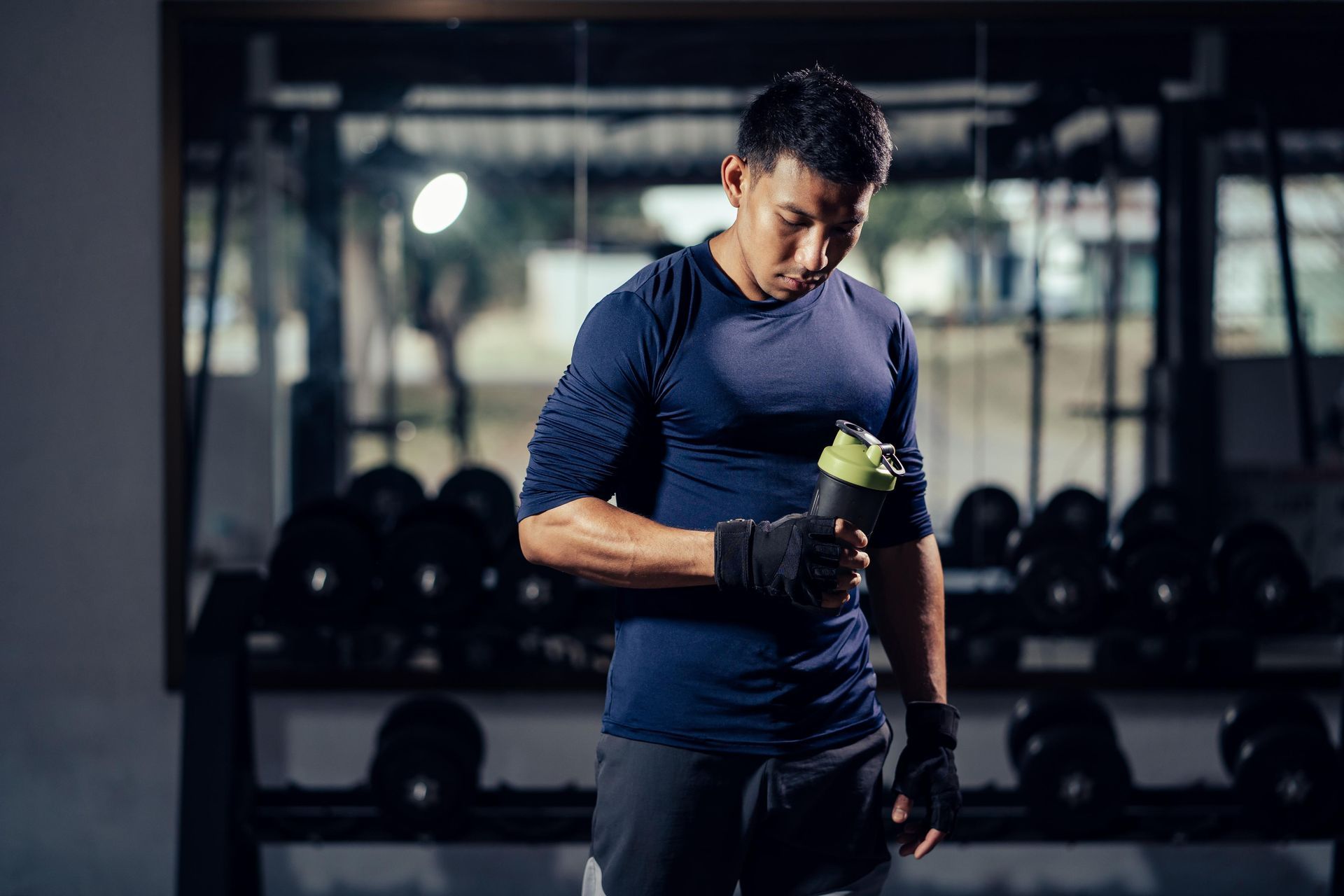 Man in gym attire holding shaker bottle, surrounded by weights.