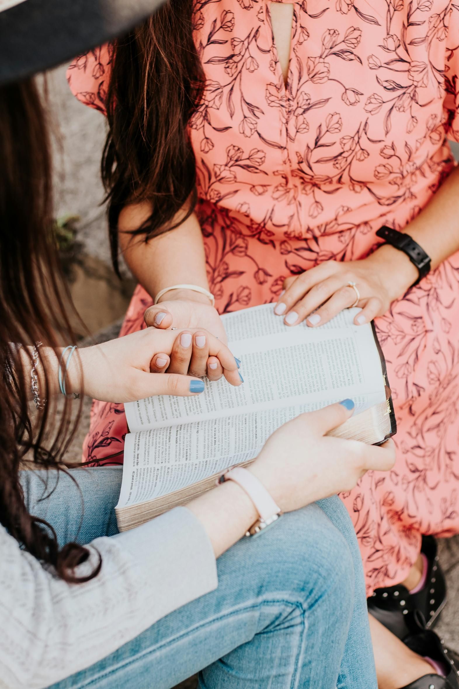 People gathered around an open book, one pointing at the text while seated outdoors.
