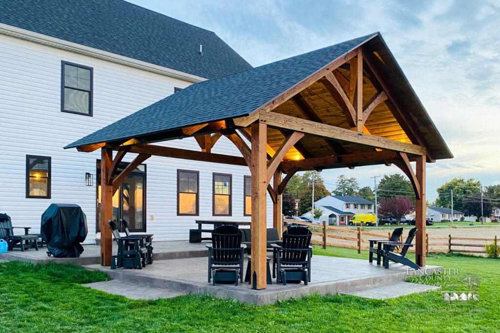 Wooden pavilion with picnic tables beside a white building at dusk