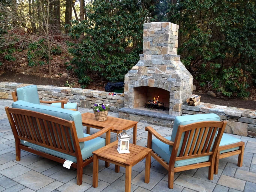Outdoor patio with wooden chairs around a stone fire pit and a low table on a paved terrace
