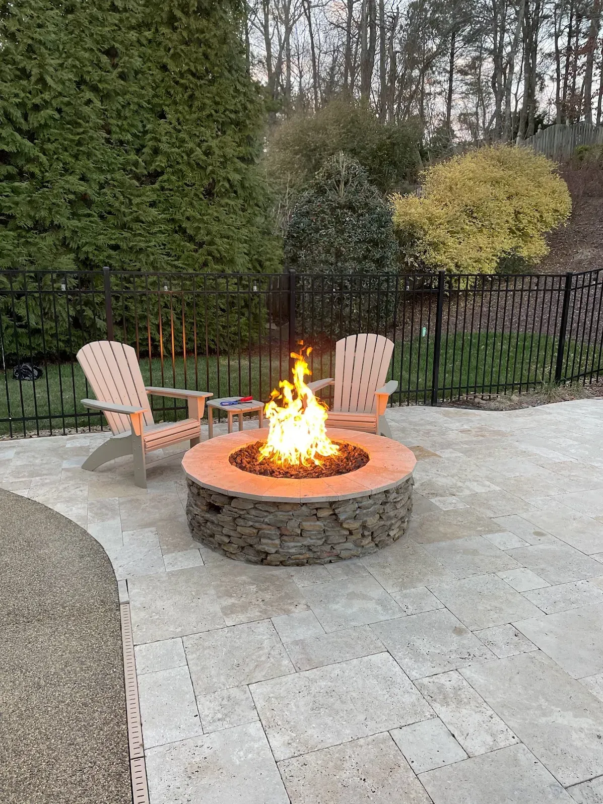 Backyard fire pit with two Adirondack chairs on a stone patio at dusk