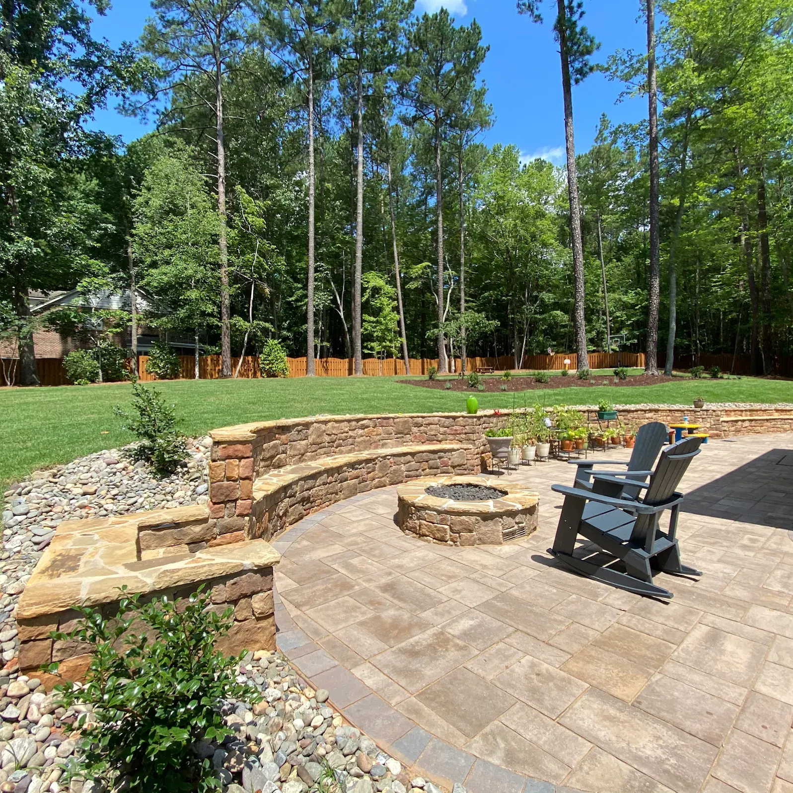 Backyard stone patio with fire pit, Adirondack chair, and wooded lawn in the background