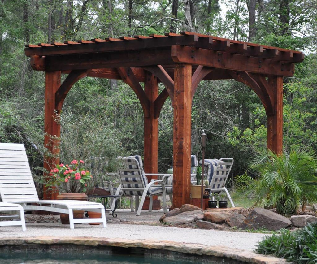 Wooden gazebo beside a pool, surrounded by white lounge chairs and lush greenery.