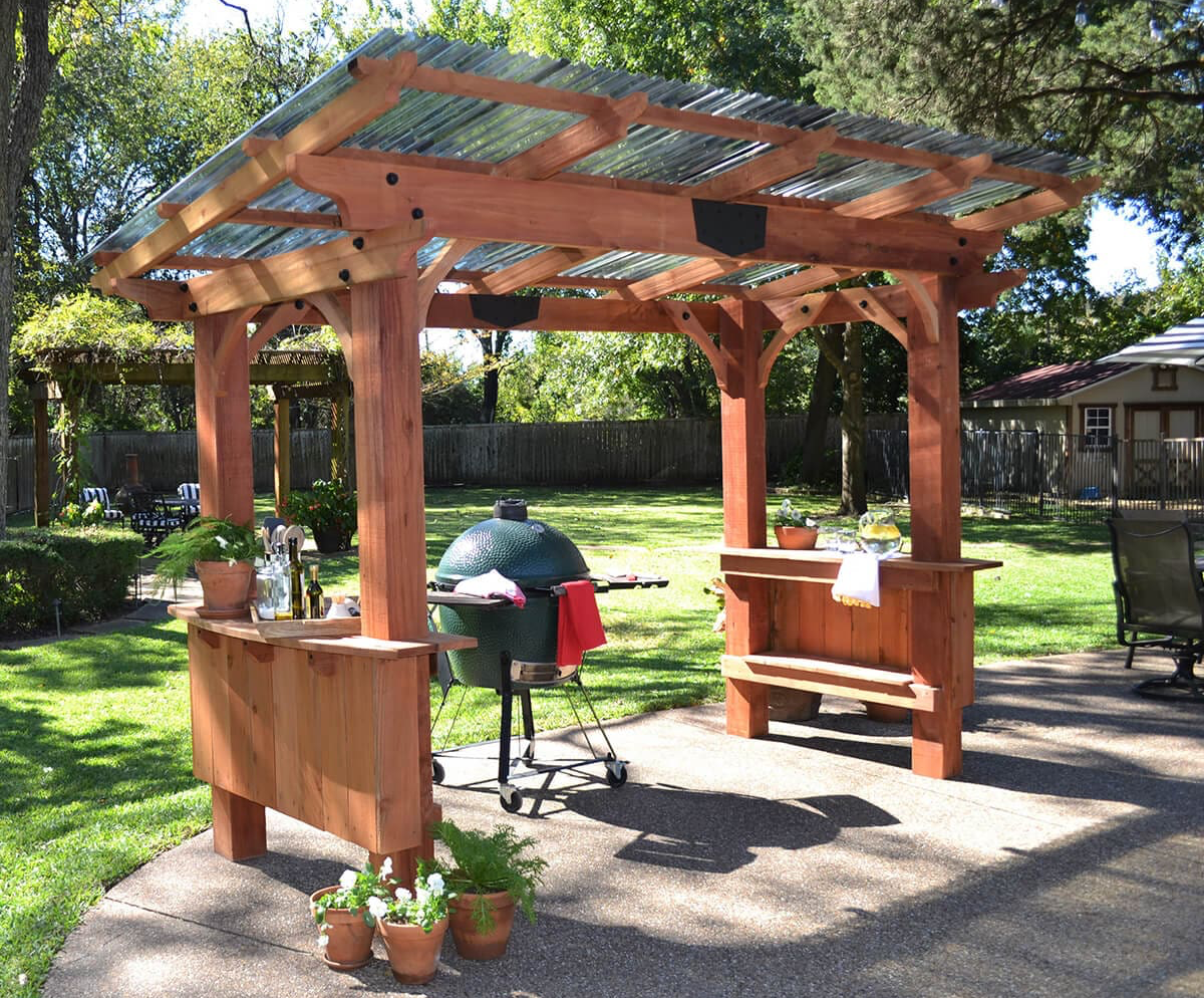 Wooden outdoor pergola with built-in benches and a green barbecue grill in a sunny yard