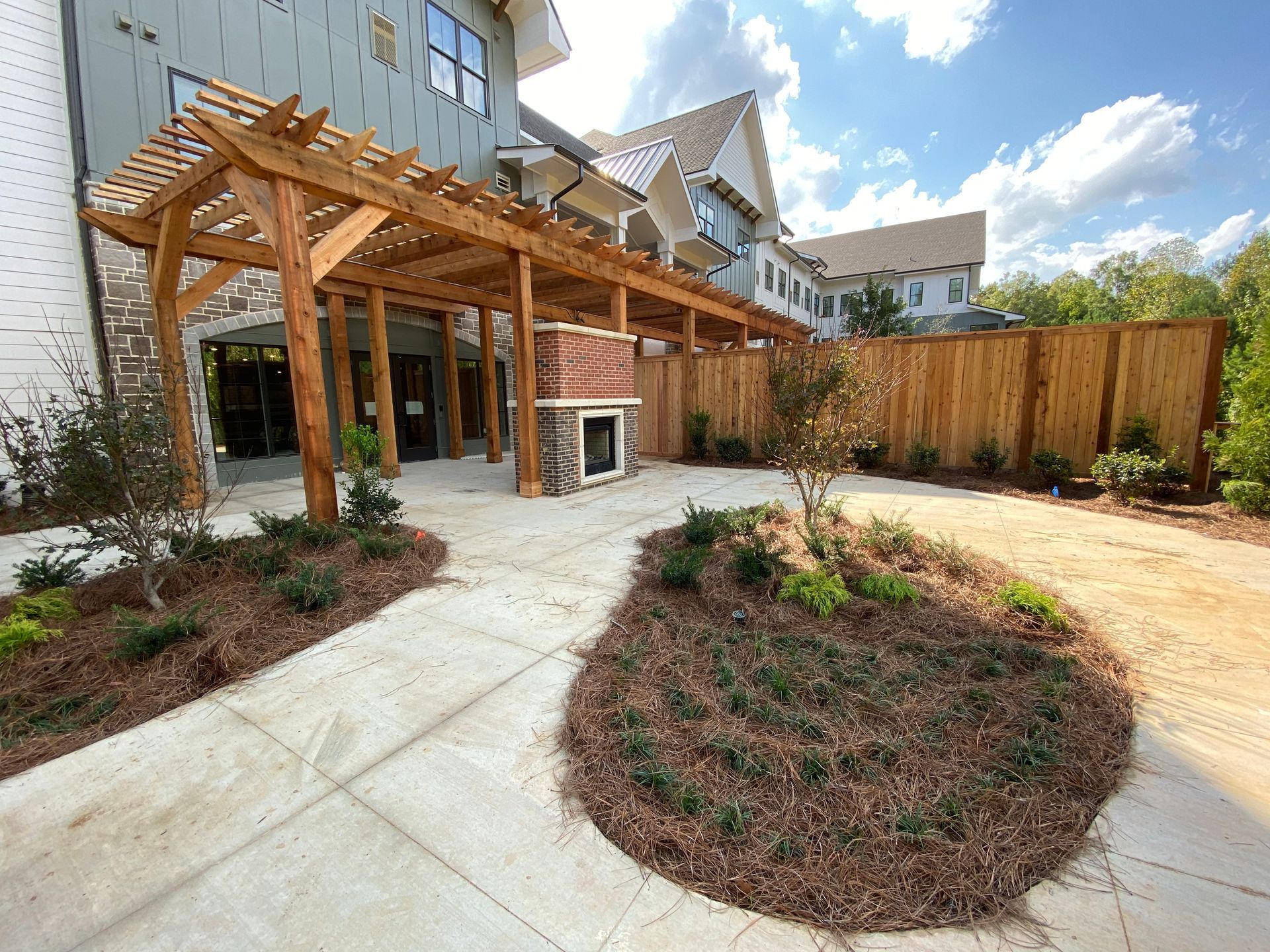Backyard patio with wooden pergola, concrete path, and landscaped garden beds beside a house