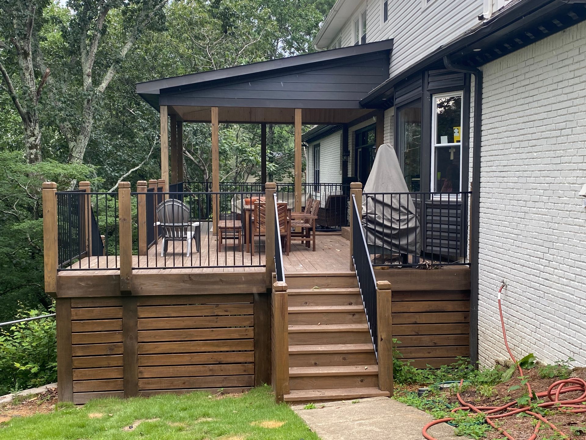 Backyard deck with steps, black railing, and covered patio beside a white house.