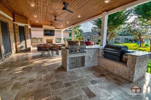 Covered patio with stone floor, wood ceiling, outdoor kitchen, dining table, and seating overlooking a yard