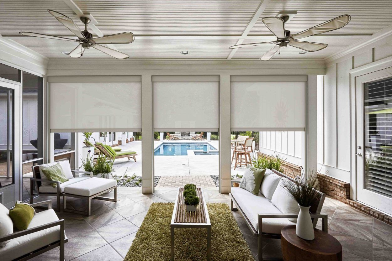Bright sunroom with white furniture, ceiling fans, and large windows overlooking a pool and patio