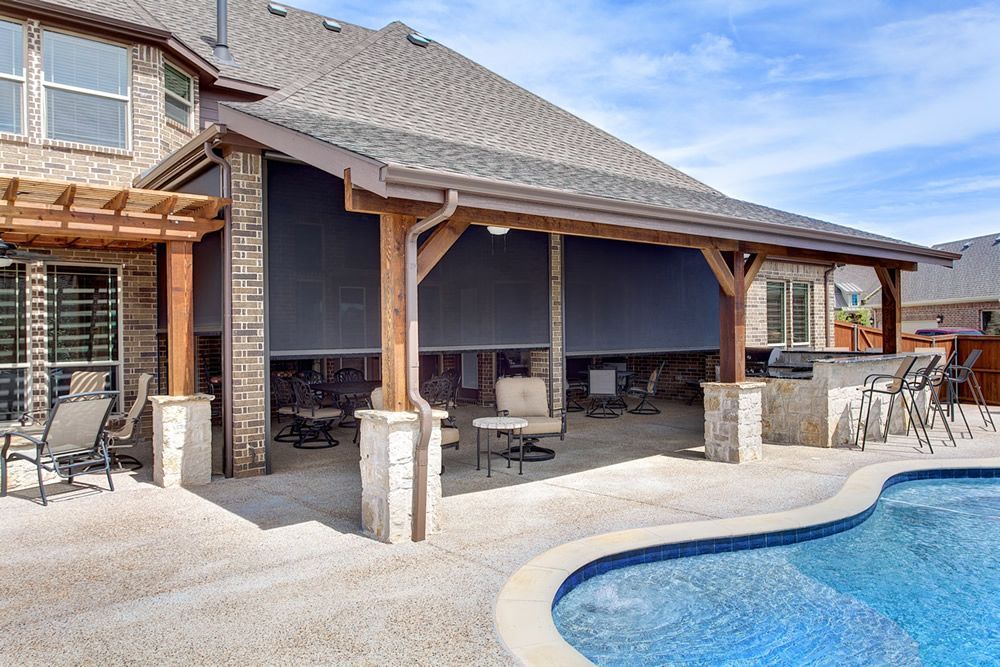 Covered patio lounge beside a backyard pool with stone columns, outdoor seating, and a screened enclosure.