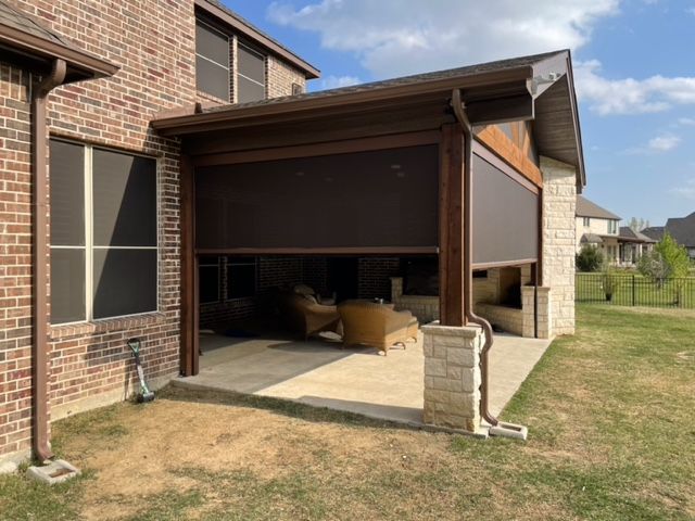 Covered patio with a raised garage-style door, concrete floor, and stored boxes beside a brick house.