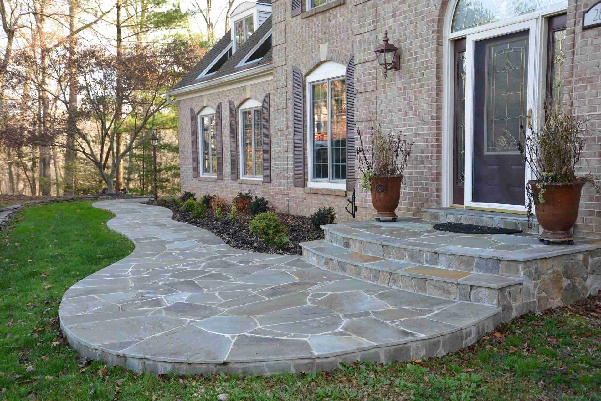 Curved flagstone walkway leading to a brick house with front steps and potted plants