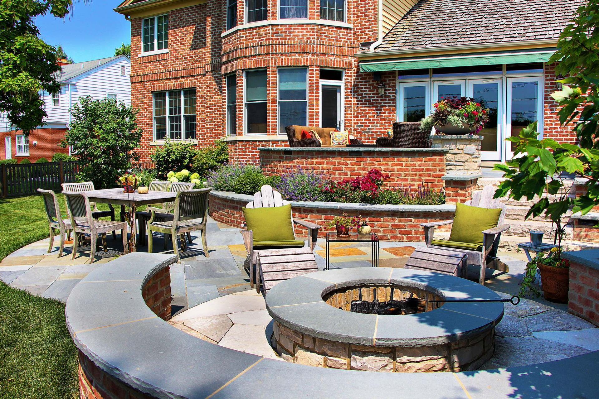 Brick patio with curved fire pit, outdoor seating, and dining table in a landscaped backyard