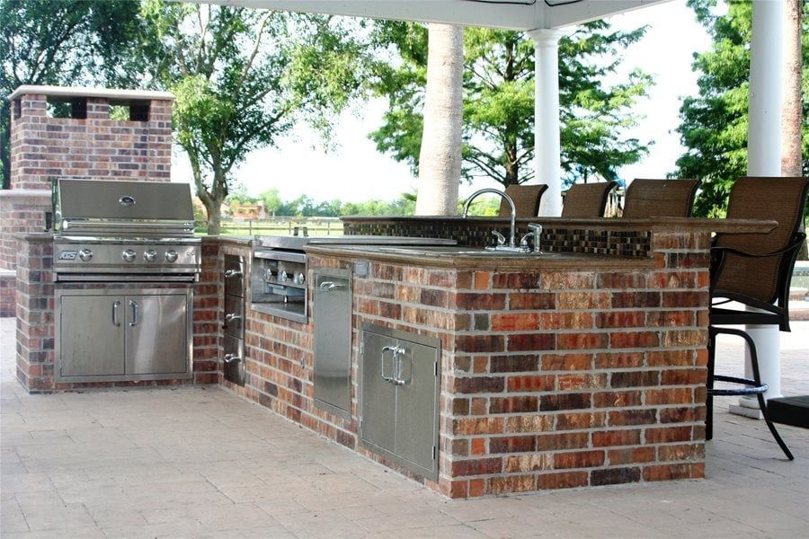 Outdoor brick patio kitchen with built-in grill, sink, and counter under a covered pavilion