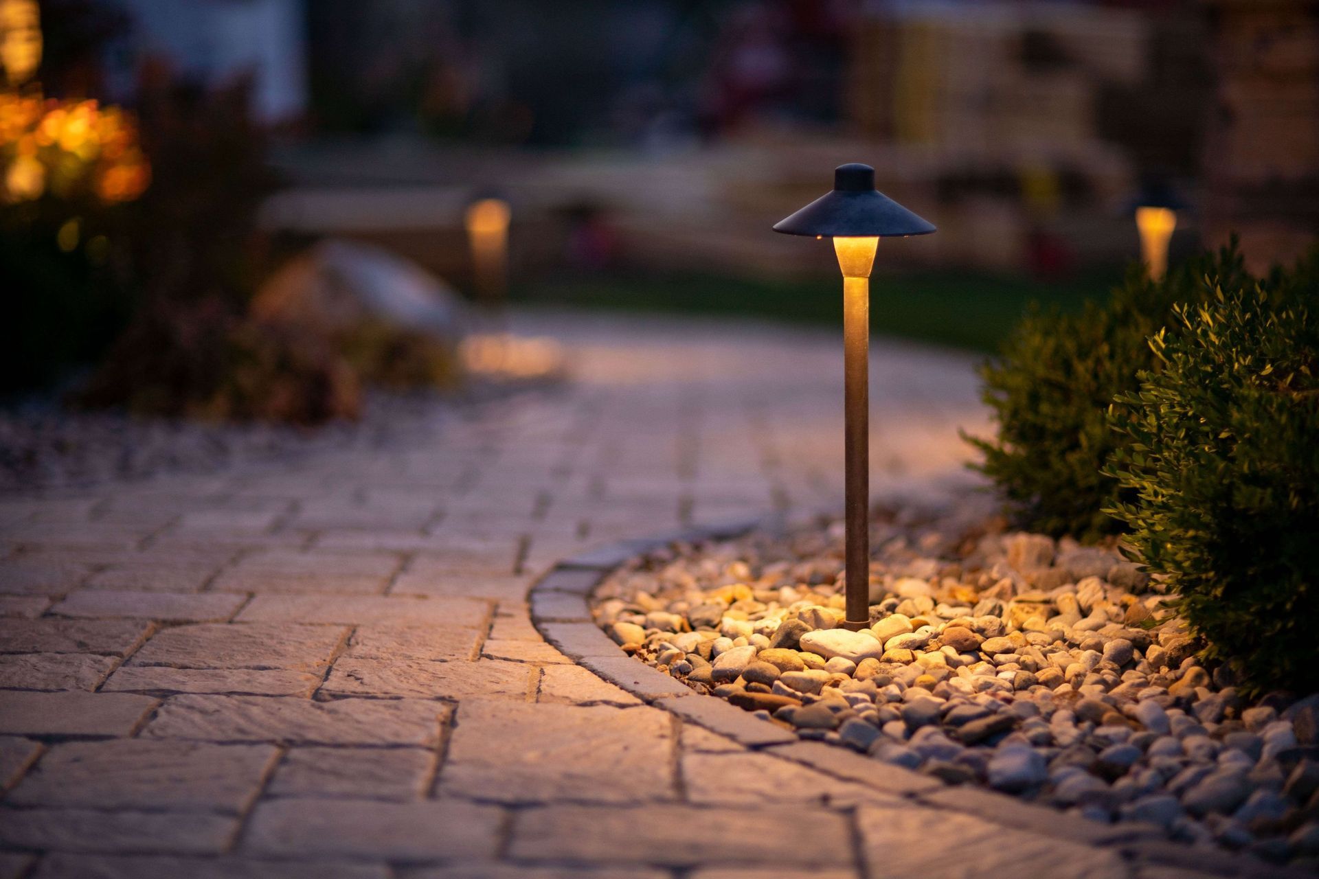 Garden path lit by a small lamp at dusk, with stone pavers and shrubs beside it