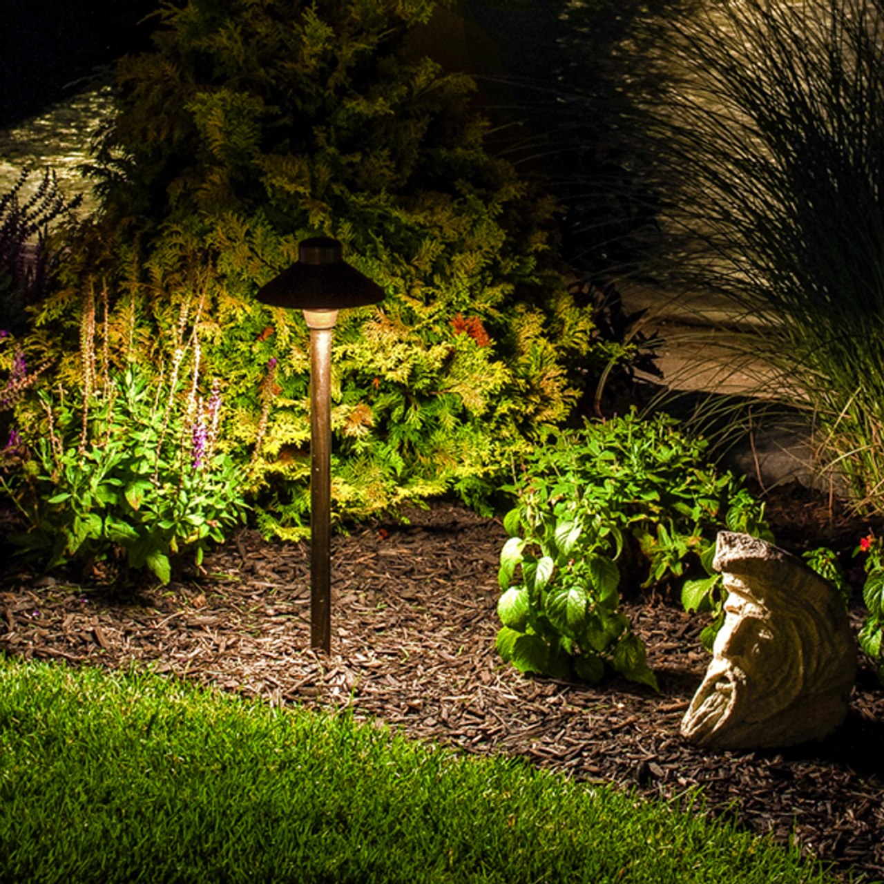 Illuminated garden bed with lush plants, a mushroom-shaped lamp, and a frog statue at night