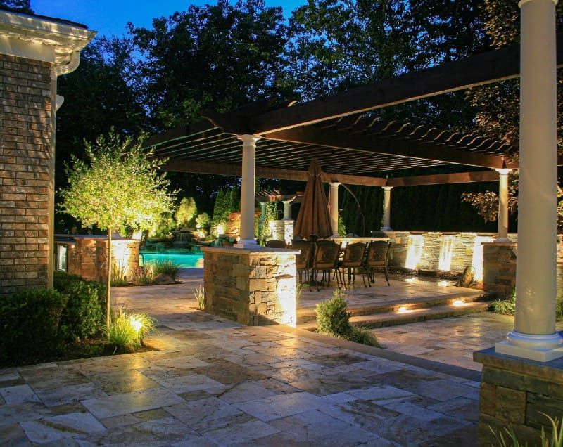 Illuminated outdoor patio with stone pillars, lounge seating, and a lit pool at dusk