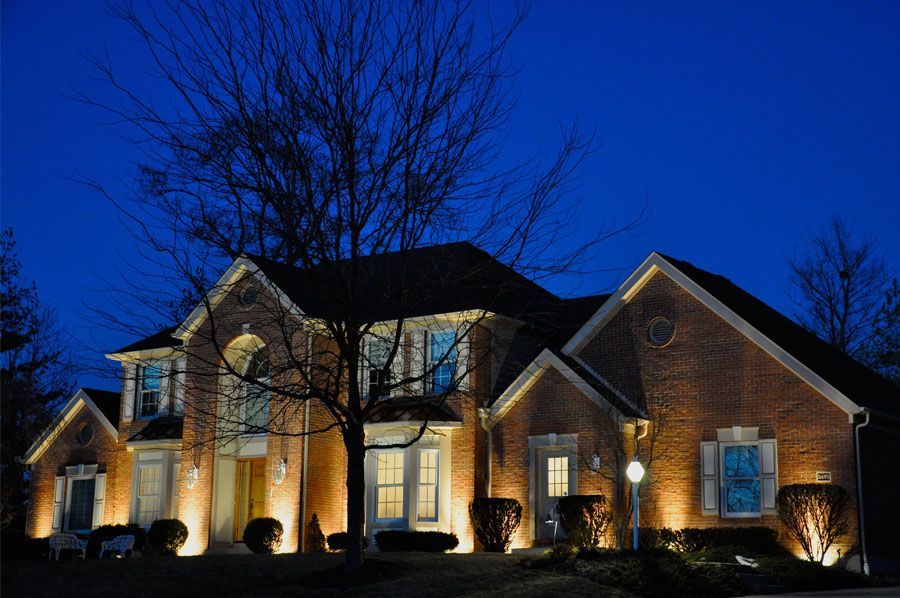 Lit brick house at dusk with warm exterior lights and a dark blue sky