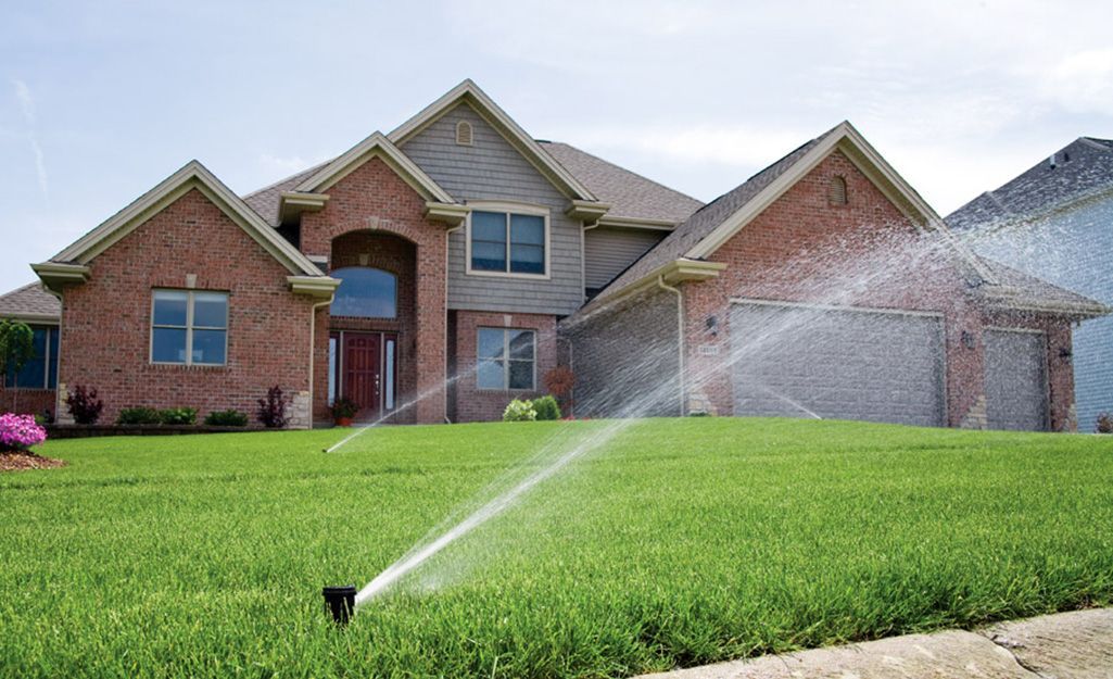 Sprinkler watering a green lawn in front of a brick suburban house
