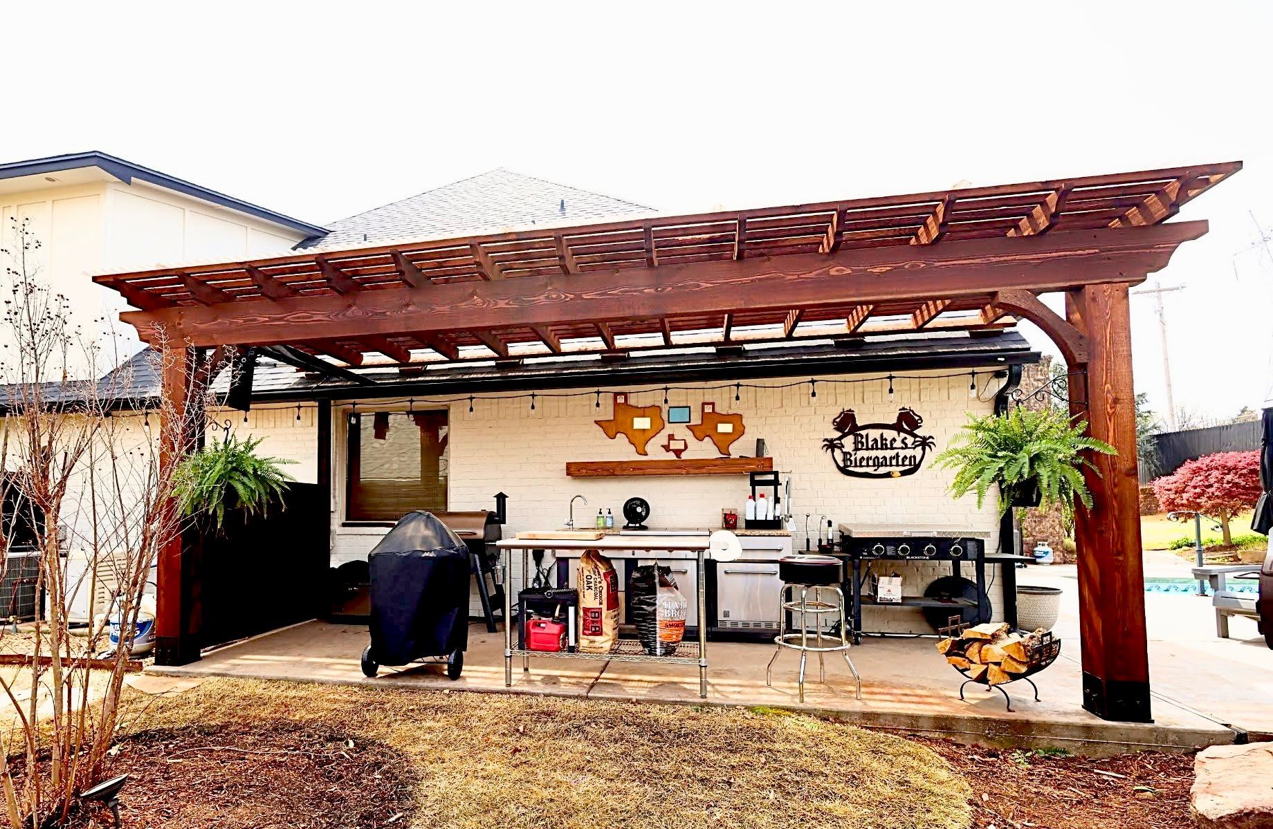 Covered outdoor patio with wooden pergola, grill, sink, and bar seating in a backyard patio setup