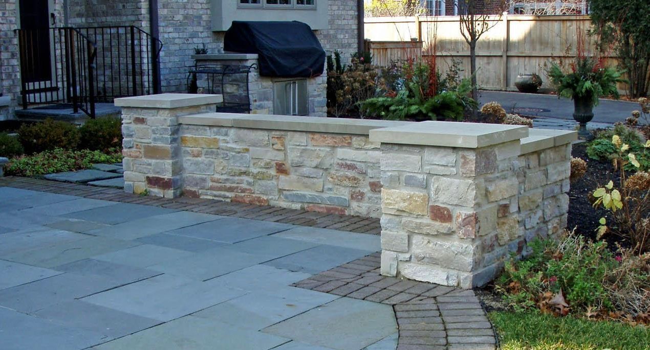 Stone planter wall beside a paved walkway in a landscaped courtyard