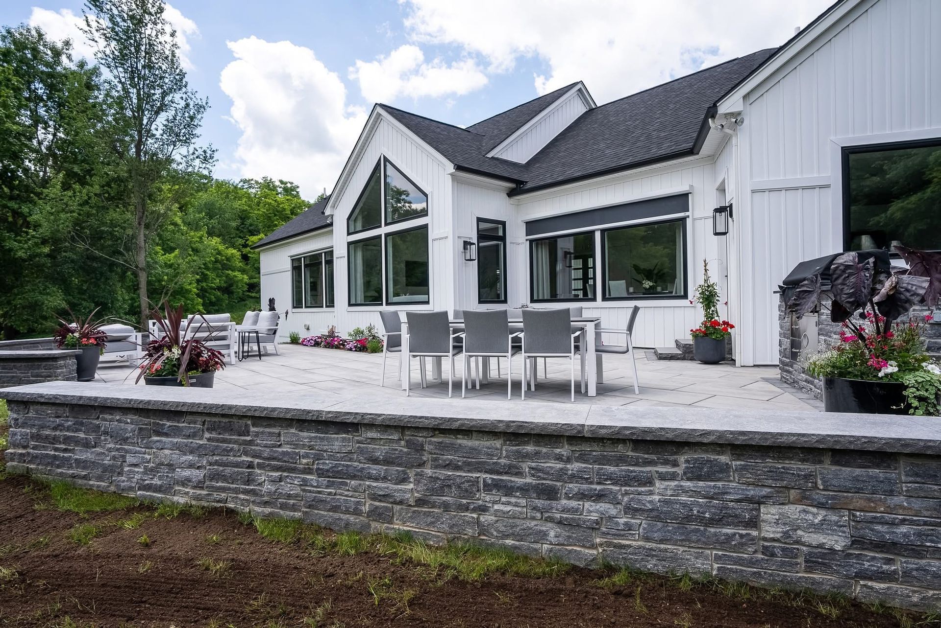 Modern white house with large windows and a stone patio overlooking a landscaped garden