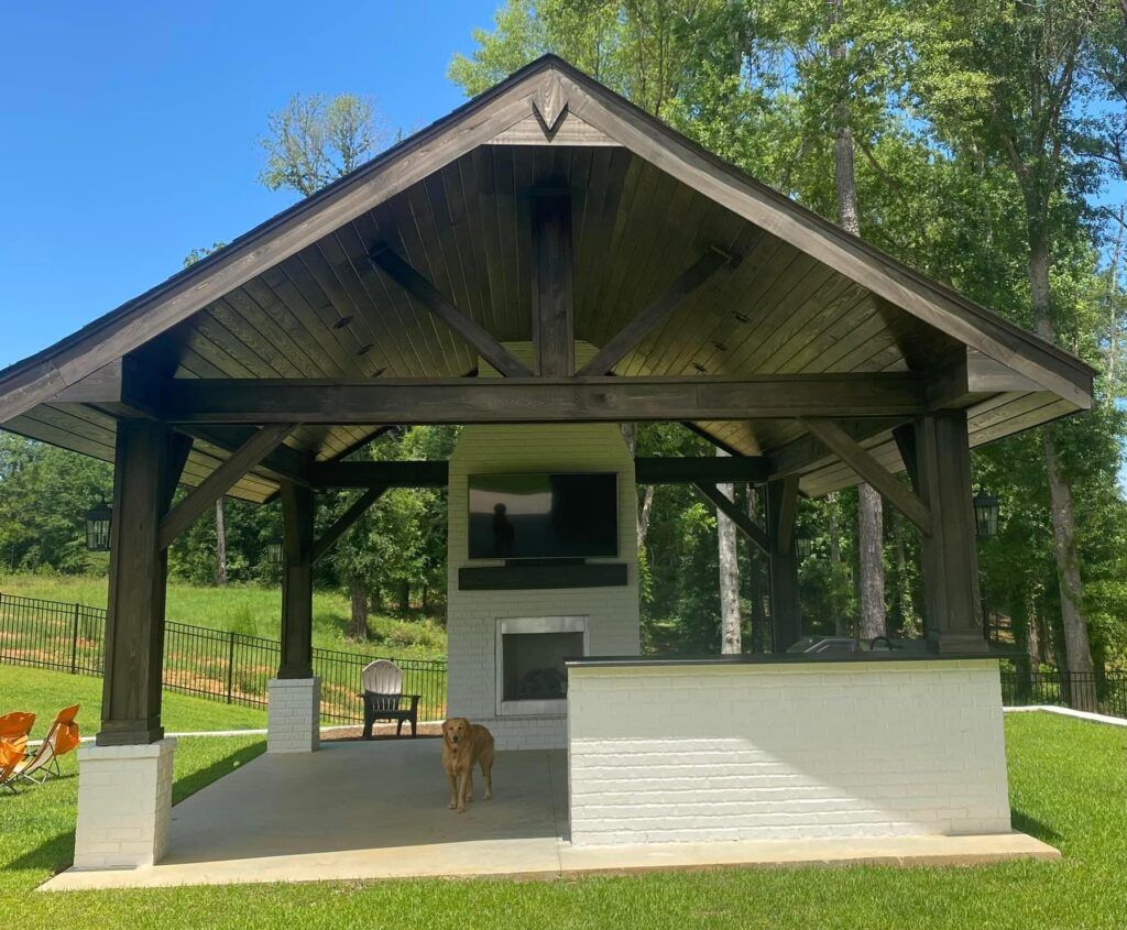 Open-air pavilion with dark wood roof and white walls in a grassy wooded yard; a deer stands inside.