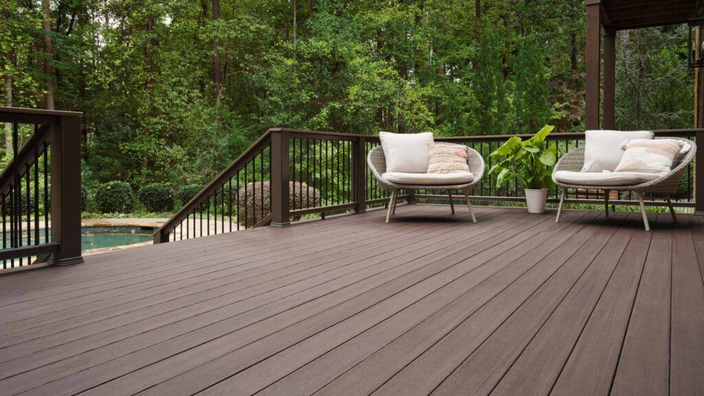 Wooden deck with two white lounge chairs overlooking a lush green forest and pond