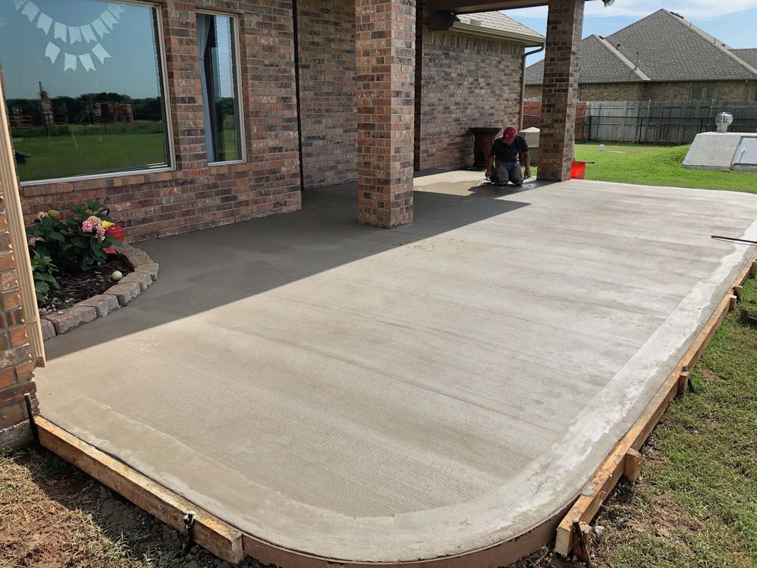 Freshly poured concrete front porch beside a brick house, with a curved edge and column supports