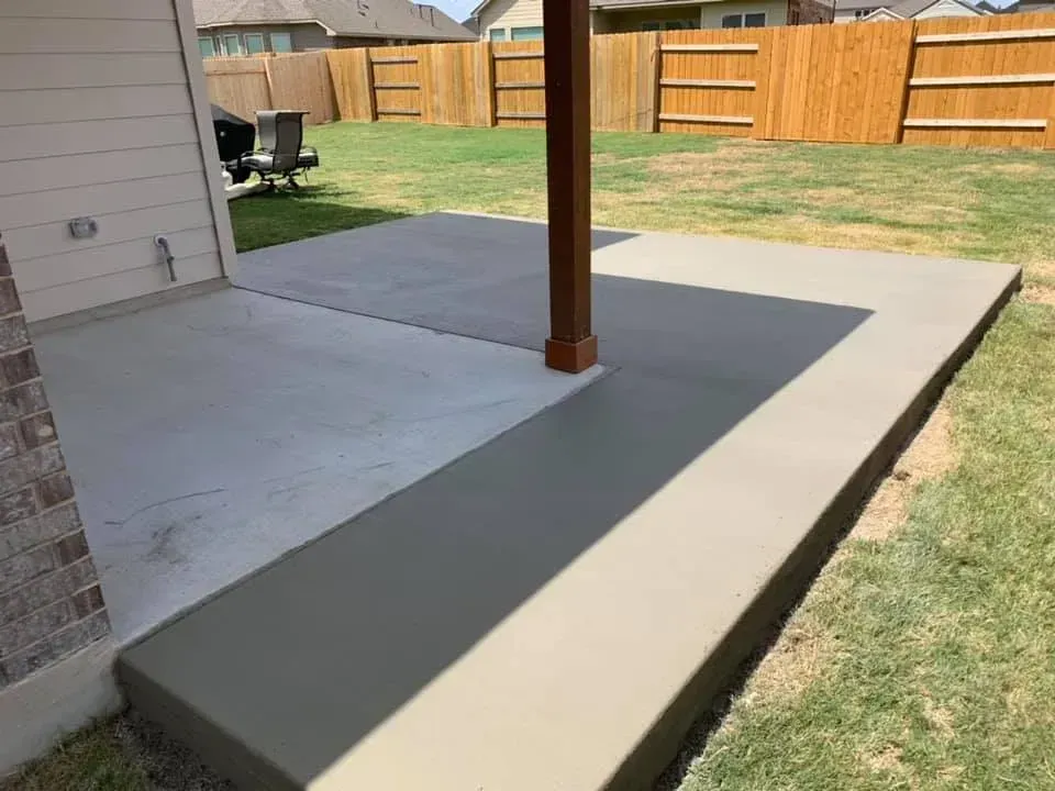 Concrete patio with a wooden support post beside a grassy yard and fenced backyard