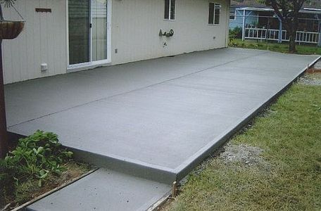 Fresh gray concrete patio beside a house, with a small step down to a walkway and yard