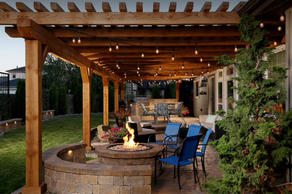 Backyard patio with pergola, string lights, stone fire pit, and blue chairs at dusk