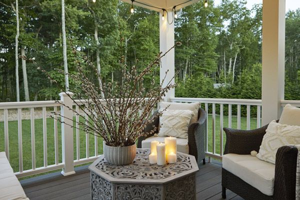 Covered porch with wicker chairs, candlelit table, and potted branches overlooking a green yard