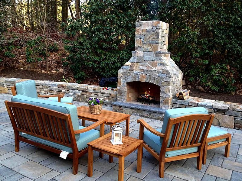 Outdoor patio with wooden seating around a stone fireplace on a paved terrace