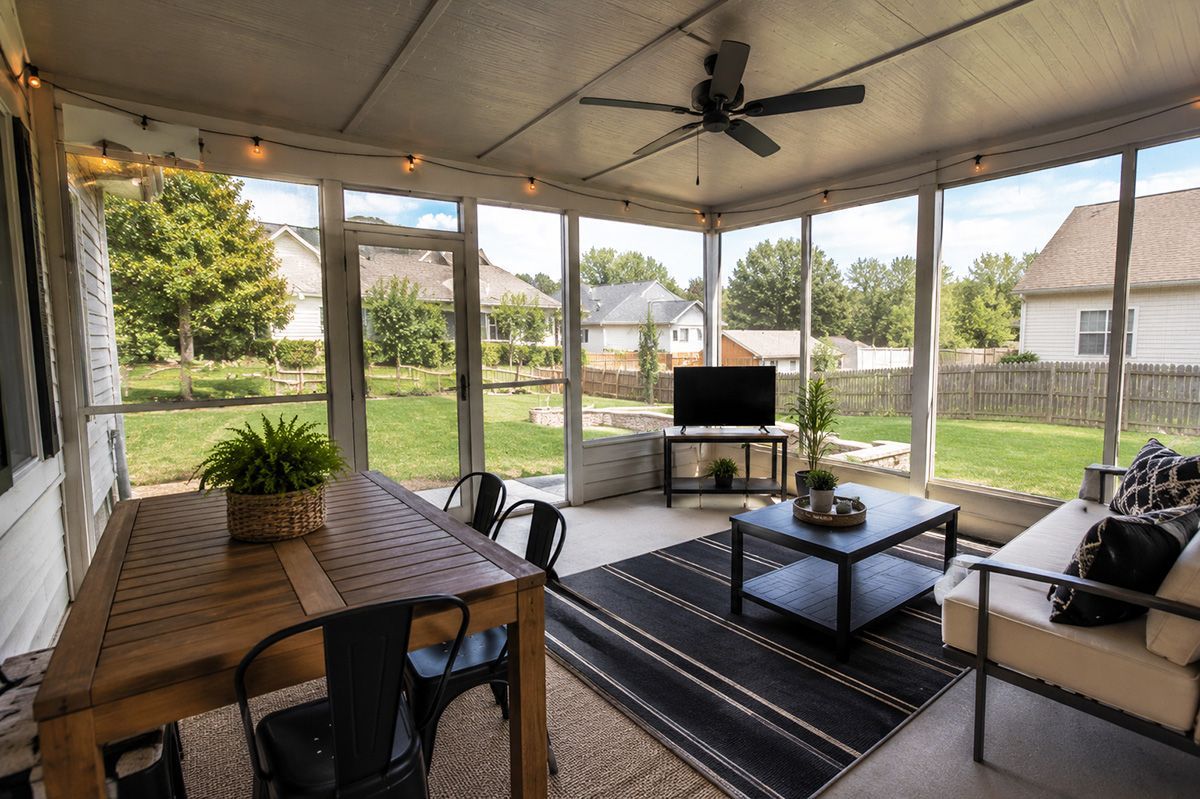 Covered patio with seating, TV, ceiling fan, and yard view through screened openings