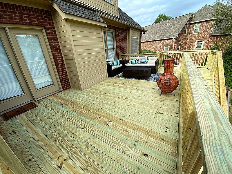 Wooden deck with patio table, chairs, and umbrella in a sunny backyard