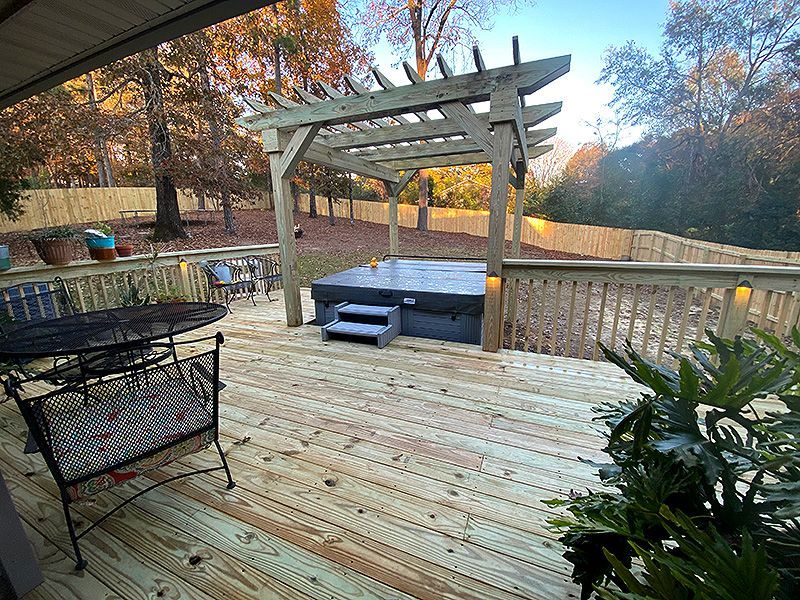 Wooden deck with pergola and hot tub, surrounded by autumn trees and railing.