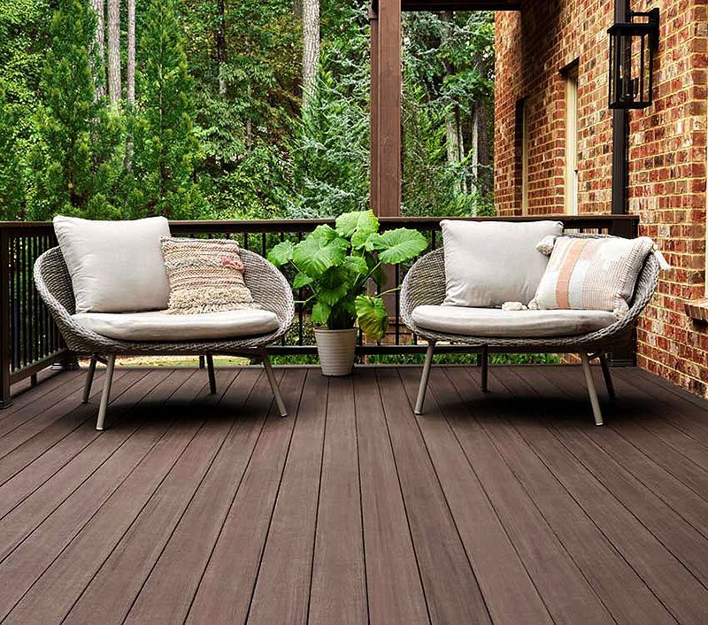Patio with two cushioned lounge chairs, potted greenery, and a brick wall beside a wooded view