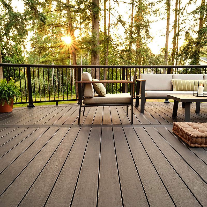 Modern wooden deck with patio seating, potted plants, and warm sunset light by a forest