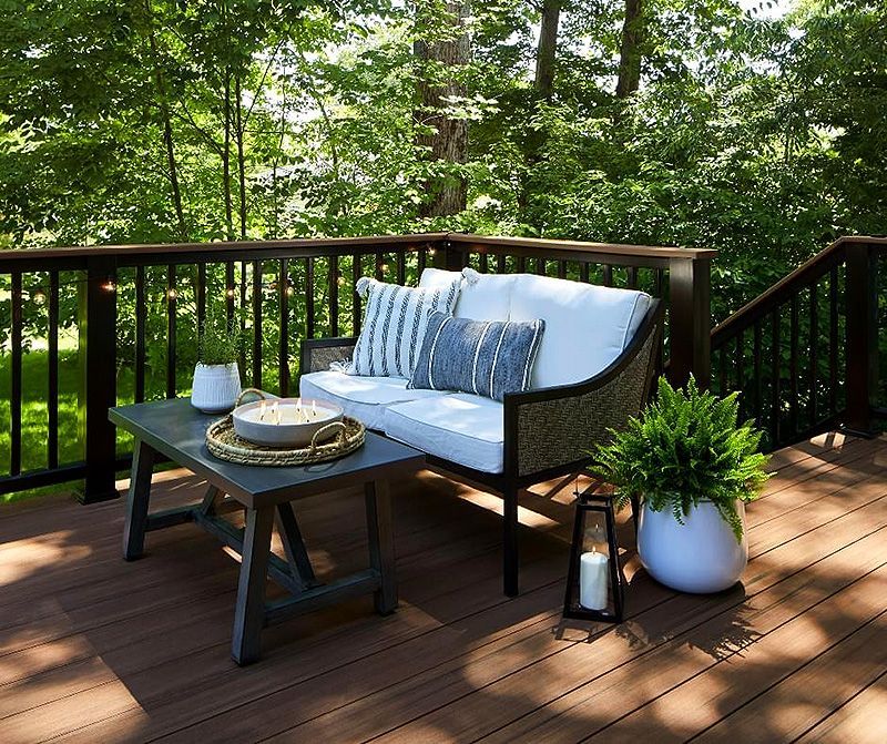 White cushioned patio bench with tray and potted plant on a wooden deck, surrounded by green trees