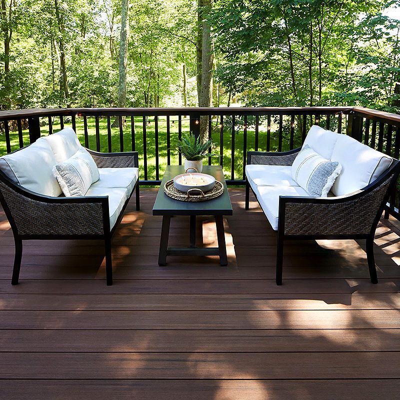 Outdoor deck with two cushioned chairs and a small table, overlooking a green wooded area.